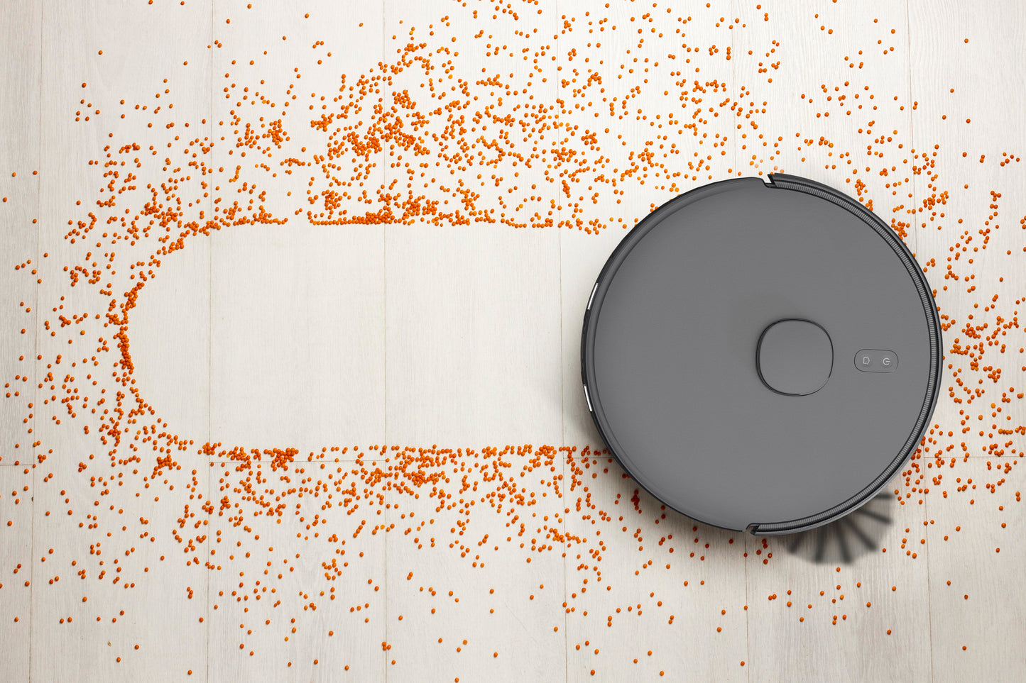 AIRROBO robot vacuum cleaner creating a clean path through scattered orange debris on light wooden floor