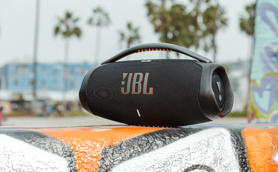 JBL Boombox 3 portable speaker placed outdoors on colorful surface with palm trees in background