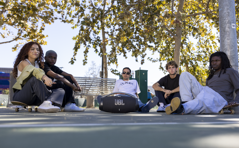 Group relaxing outdoors with JBL Boombox 3 speaker on ground under autumn trees