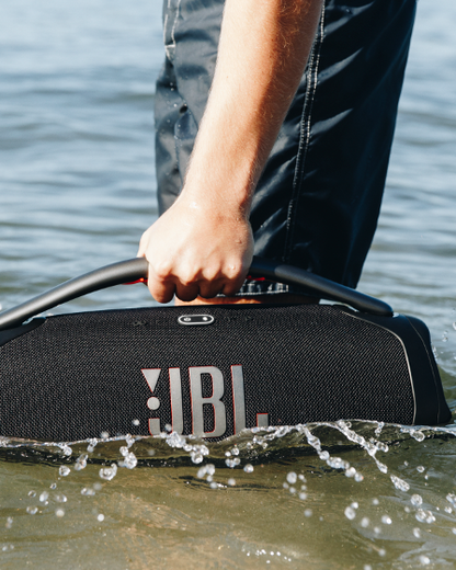 JBL Boombox 3 portable speaker splashing in water, demonstrating waterproof features with handle grip