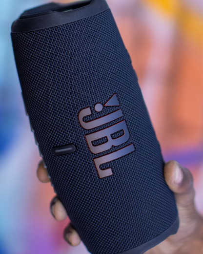 JBL Charge 5 portable speaker in black with textured mesh finish and prominent JBL logo against colorful background