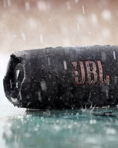 JBL Charge 5 portable speaker in black, water-resistant design shown in rain with water droplets on its surface